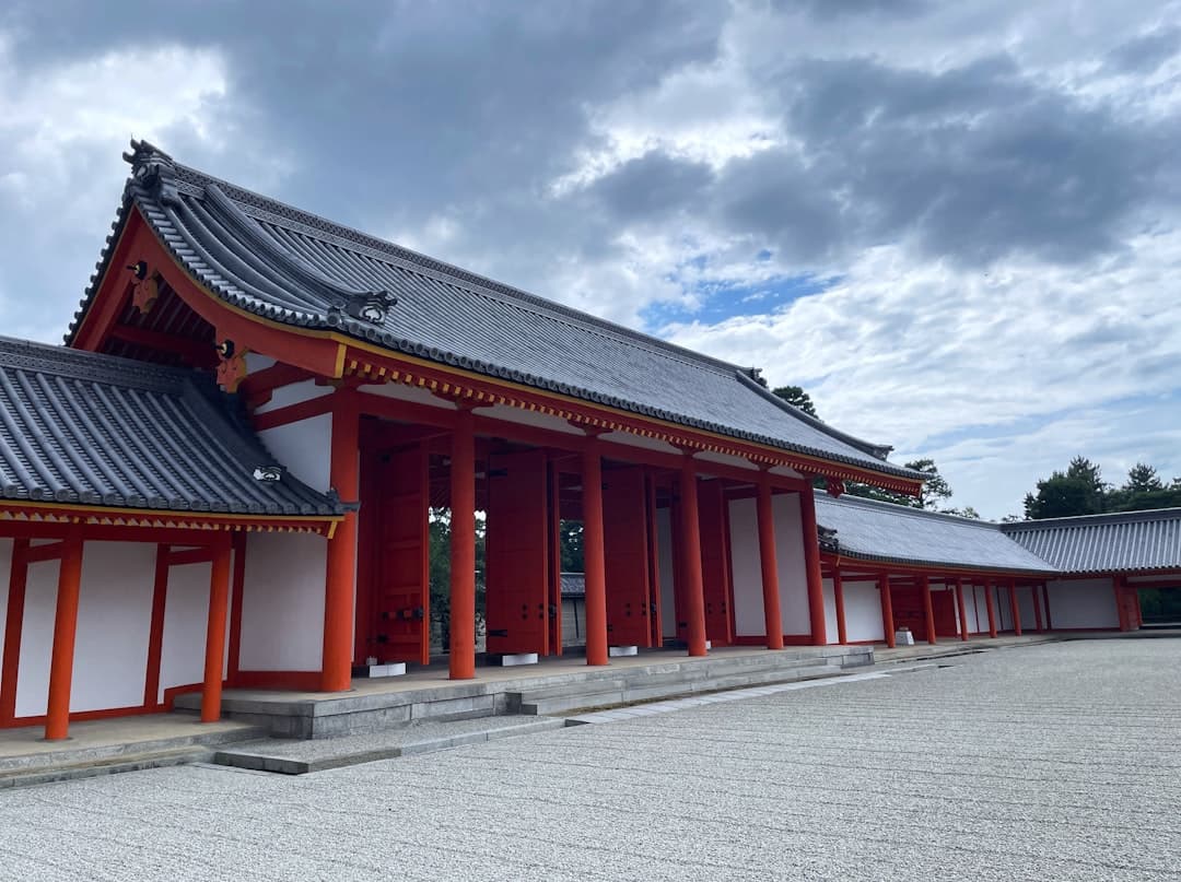 A traditional Japanese temple complex featuring red pillars and white walls with characteristic curved tile roofs and ornamental details. - Photo by Ronin on Unsplash