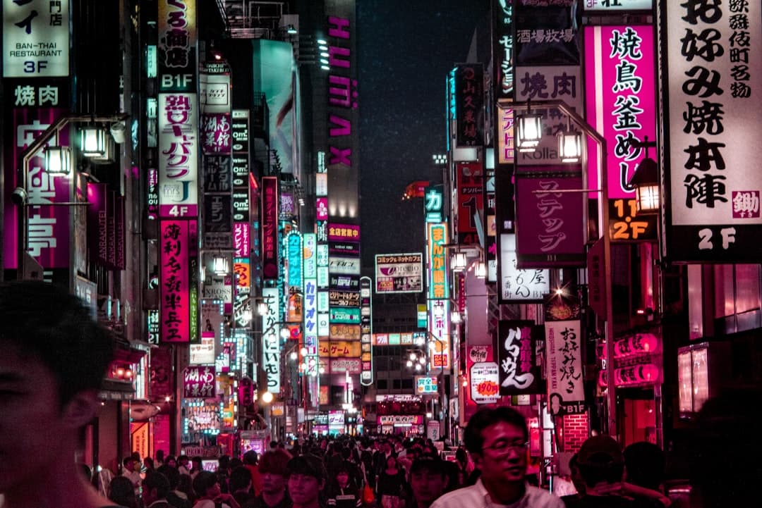 A vibrant nighttime street scene in a densely packed urban entertainment district filled with neon signs in Japanese characters, crowded with pedestrians, featuring magenta and cyan neon lighting dominating storefronts and signage. - Photo by ALEXANDRE LALLEMAND on Unsplash