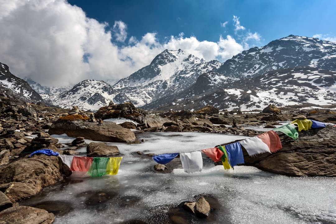A high-altitude alpine stream with prayer flags stretched across rocky terrain, backed by snow-capped Himalayan peaks under partly cloudy sky. - Photo by Sergey Pesterev on Unsplash