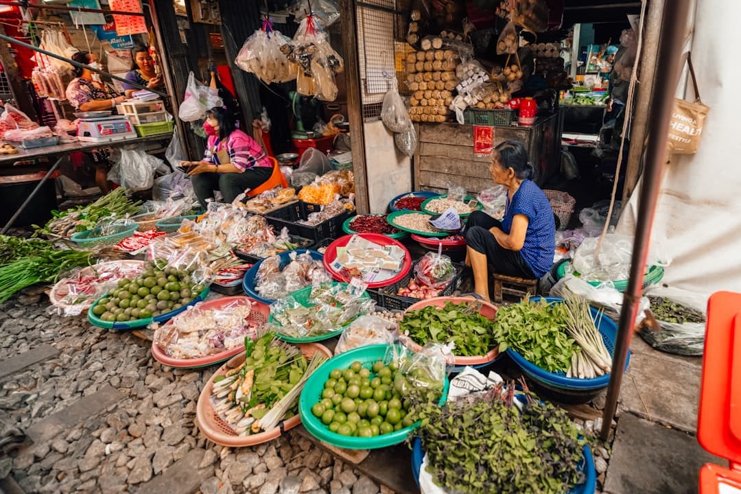 A busy open-air wet market stall with vendors selling fresh produce, herbs, and prepared foods in colorful plastic basins and trays, typical of Southeast Asian street markets. - Photo by Mauro Lima on Unsplash