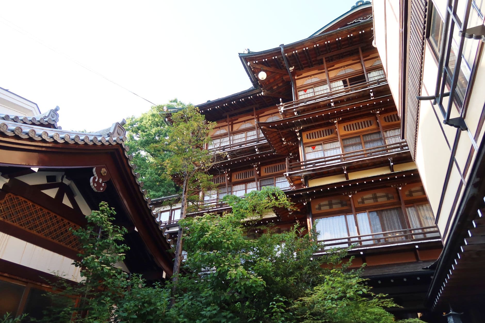 A traditional Japanese ryokan with multi-level wooden architecture, featuring dark timber construction, latticed windows, and metal railings, set within a lush garden courtyard viewed from an interior courtyard perspective. - Photo by Hiroko Nakagawa on Pexels