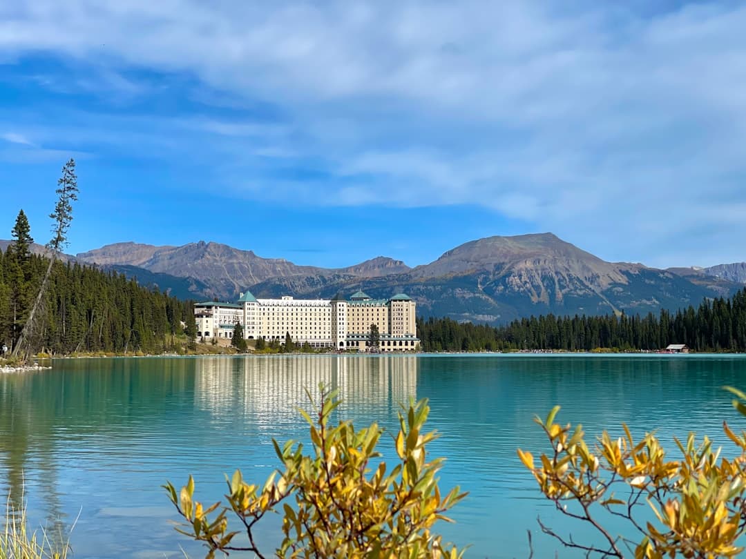 A wide view across the turquoise waters of Lake Louise toward the Fairmont Chateau Lake Louise hotel backed by snow-capped mountain peaks, with coniferous forest lining the shores. - Photo by Mahesh Gupta on Unsplash