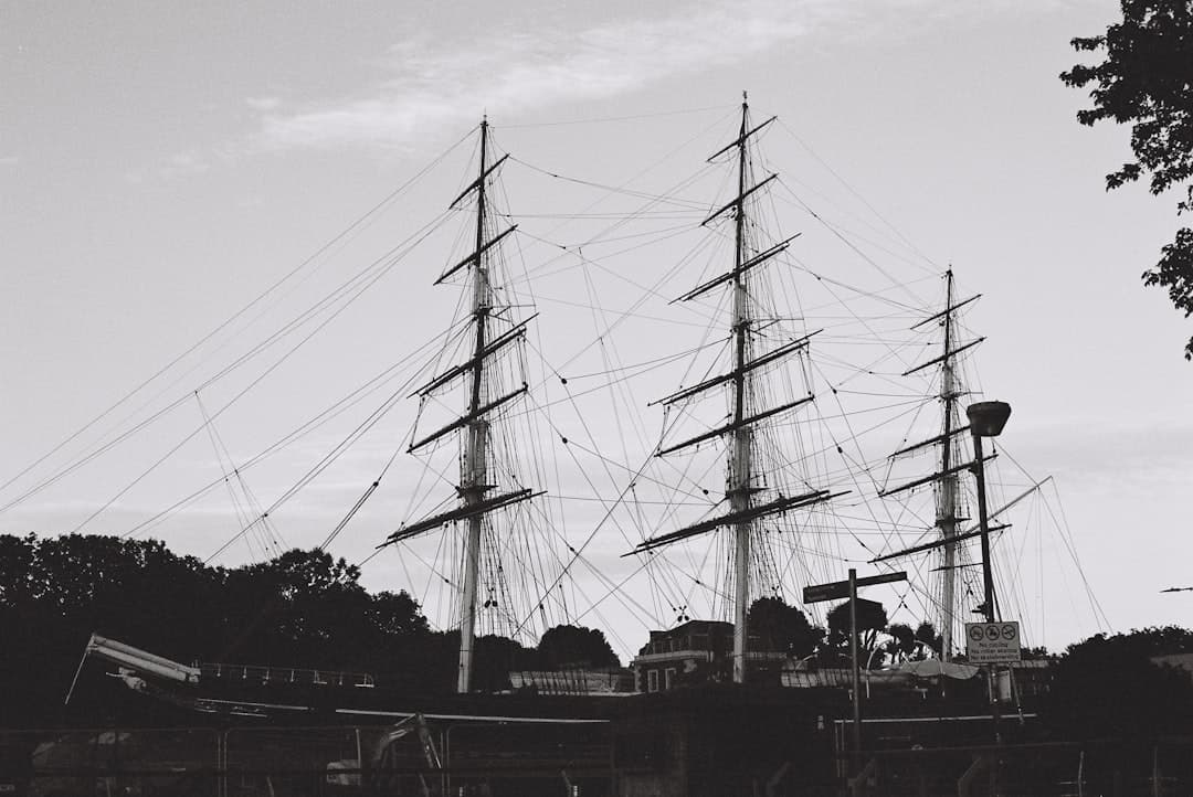 A black and white photograph of the Cutty Sark, a historic three-masted clipper ship moored at Greenwich, showing the vessel's complex rigging and masts against a cloudy sky. - Photo by T on Unsplash