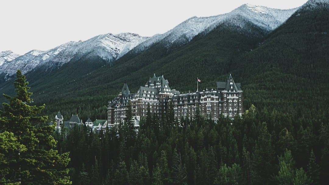 A grand castle-style hotel nestled in a forested valley with snow-capped Rocky Mountain peaks rising behind it. - Photo by Felipe Souza on Unsplash