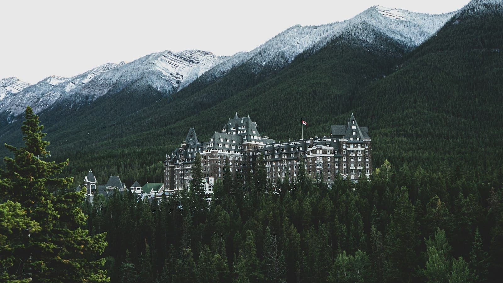 The Fairmont Banff Springs Hotel, a grand château-style building nestled in a forested valley with snow-capped Rocky Mountains rising behind it. - Photo by Felipe Souza on Unsplash