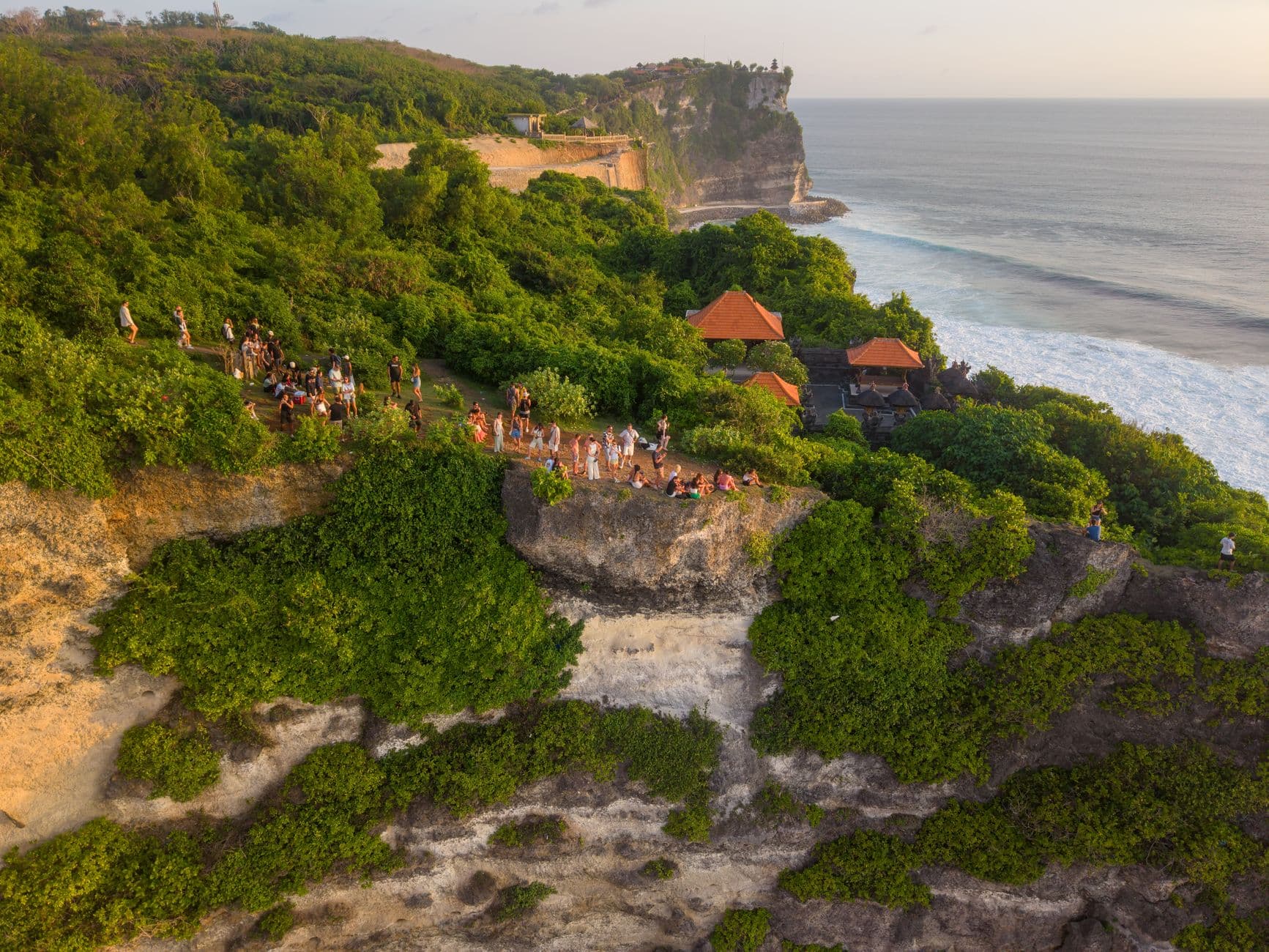 A clifftop ceremonial or gathering space in Bali with traditional Balinese pavilions featuring orange-tiled roofs, populated with visitors on a dramatic coastal outcrop overlooking the Indian Ocean. - Photo by Tom Fisk on Pexels