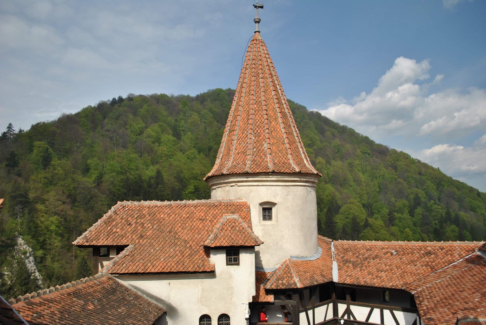 A fortified Saxon church in Transylvania featuring a central cylindrical tower with a steep conical red-tiled roof, white-washed walls, and surrounding timber-frame buildings set against forested Carpathian foothills. - Photo by Valeria Drozdova on Pexels