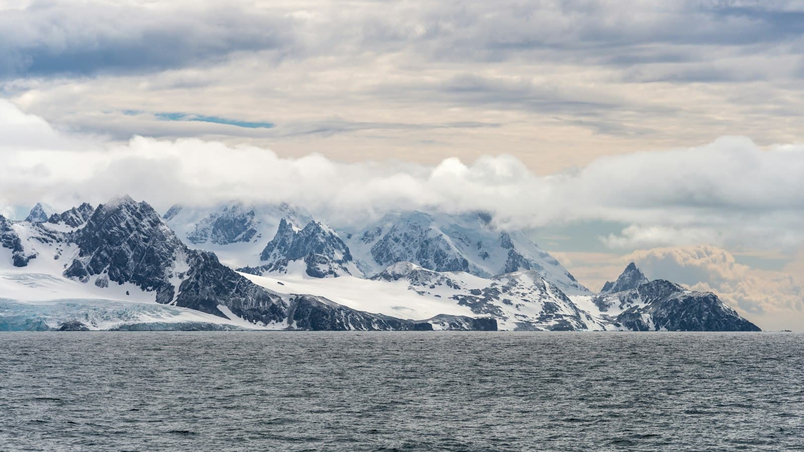 Snow-covered, dramatically jagged mountainous peaks rising from the Southern Ocean, photographed from a vessel offshore, showing the distinctive glaciated terrain of Elephant Island. - Photo by Paul Carroll on Unsplash