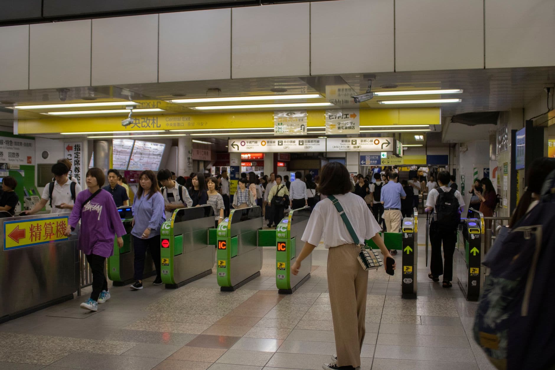 A crowded Japanese railway station concourse with passengers moving through green IC card-compatible ticket gates, with yellow accent lighting and bilingual (Japanese) signage visible. - Photo by Imani Williams on Pexels