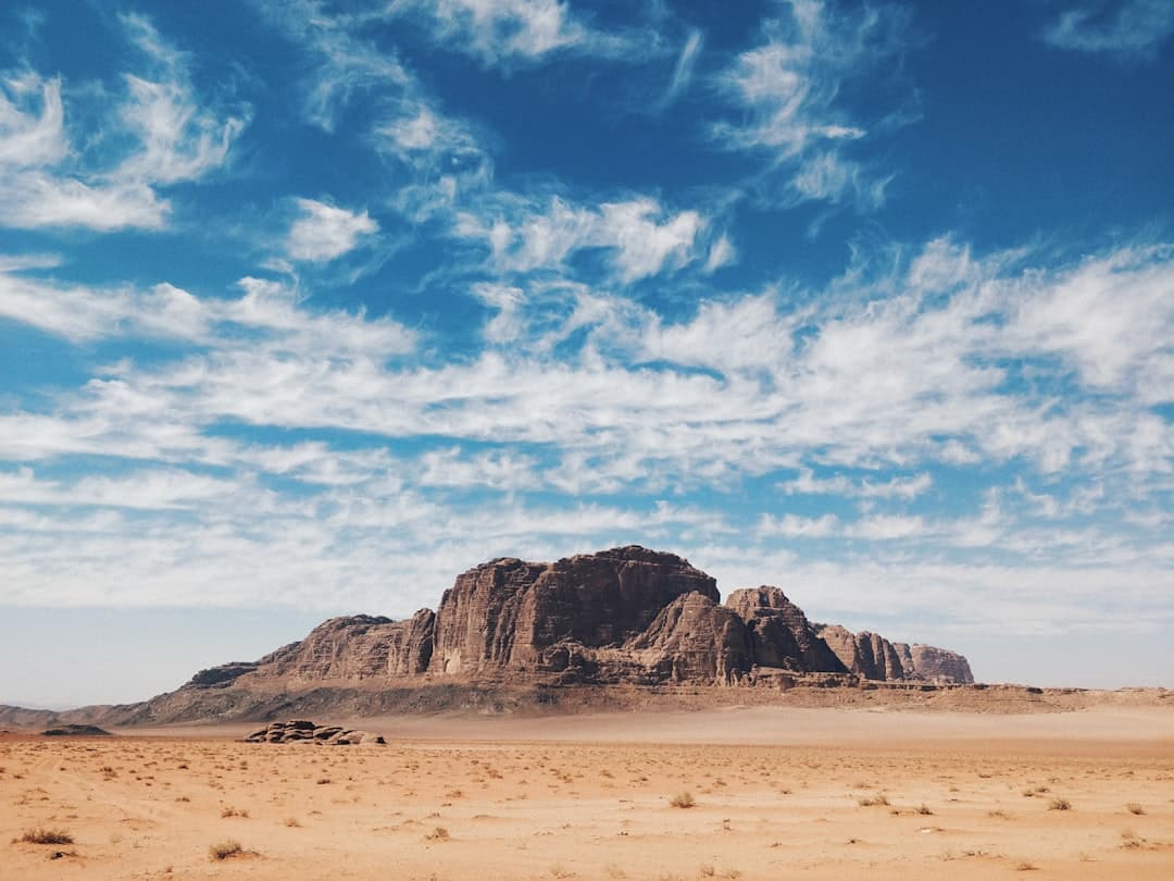 A vast desert landscape with towering sandstone buttes and rock formations rising from arid, sandy terrain beneath a partly cloudy sky. - Photo by Anton Lecock on Unsplash