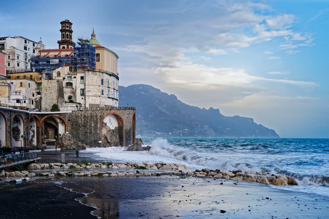 A picturesque coastal village church built directly against limestone cliffs overlooking the Tyrrhenian Sea, with traditional Mediterranean architecture and a dramatic rocky shoreline, clearly depicting the Amalfi Coast. - Photo by Gregory Smirnov on Unsplash