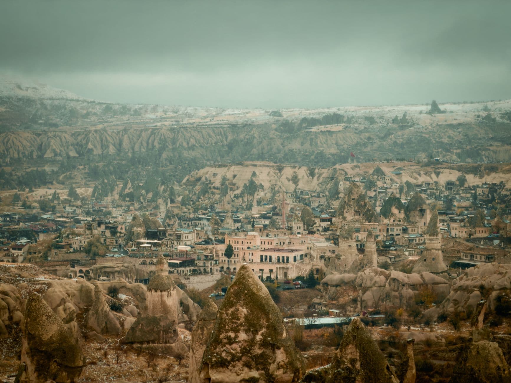 An elevated view of a town nestled among distinctive cone-shaped rock formations with cave dwellings, showing traditional architecture and a minaret amid the unique Cappadocian landscape. - Photo by Enes Haciabbasoglu on Pexels