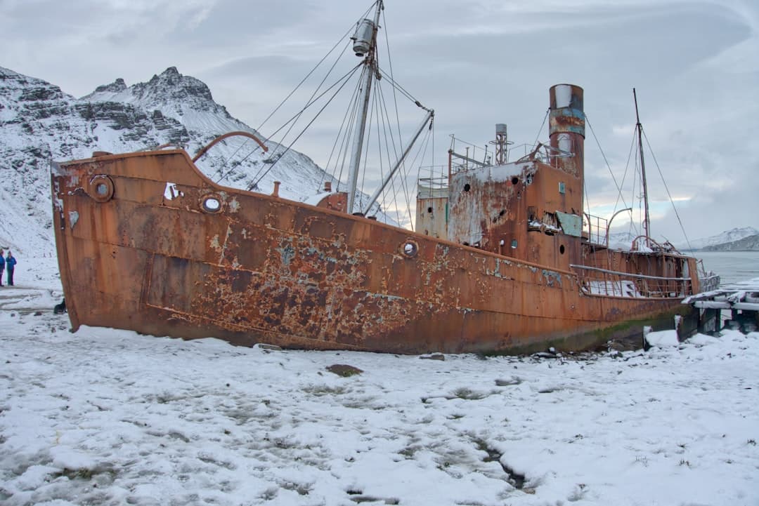 A heavily rusted, abandoned ship beached on snow-covered sand with mountainous terrain in the background, characteristic of the historic Shackleton wreck at Grytviken, South Georgia. - Photo by Graham Meyer on Unsplash