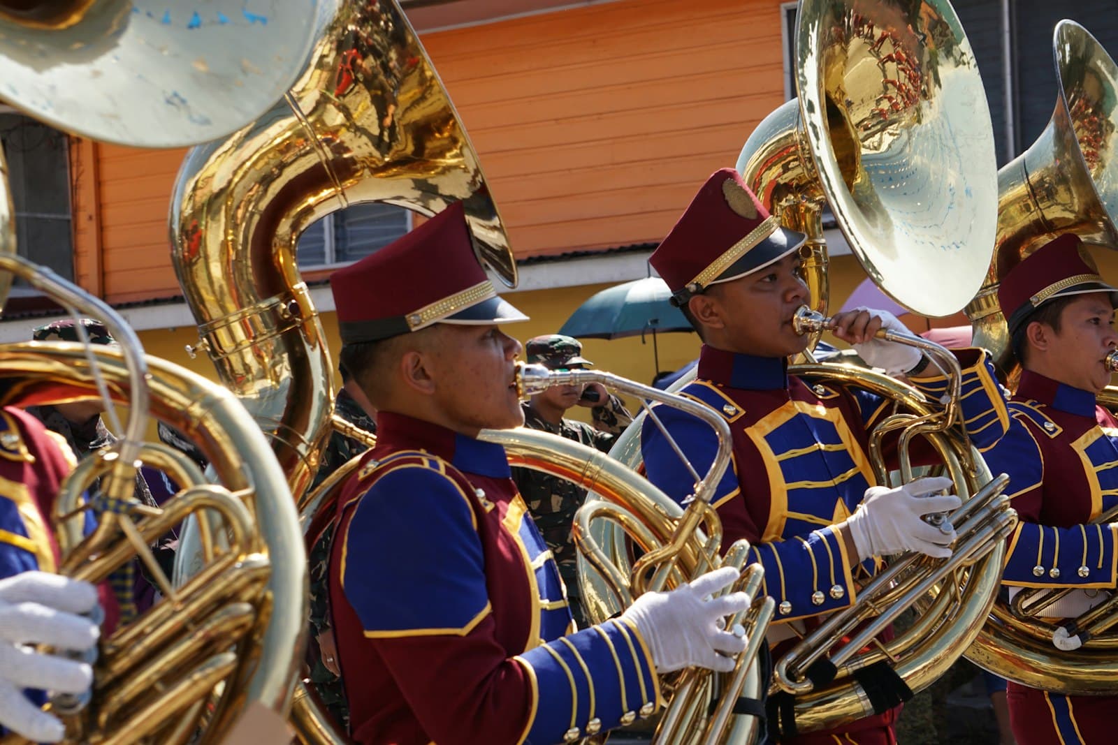 Brass band musicians in traditional Serbian festival uniforms with maroon fez hats and blue jackets with gold trim play large brass instruments including tubas during what appears to be a street performance or parade. - Photo by Beth Macdonald on Unsplash