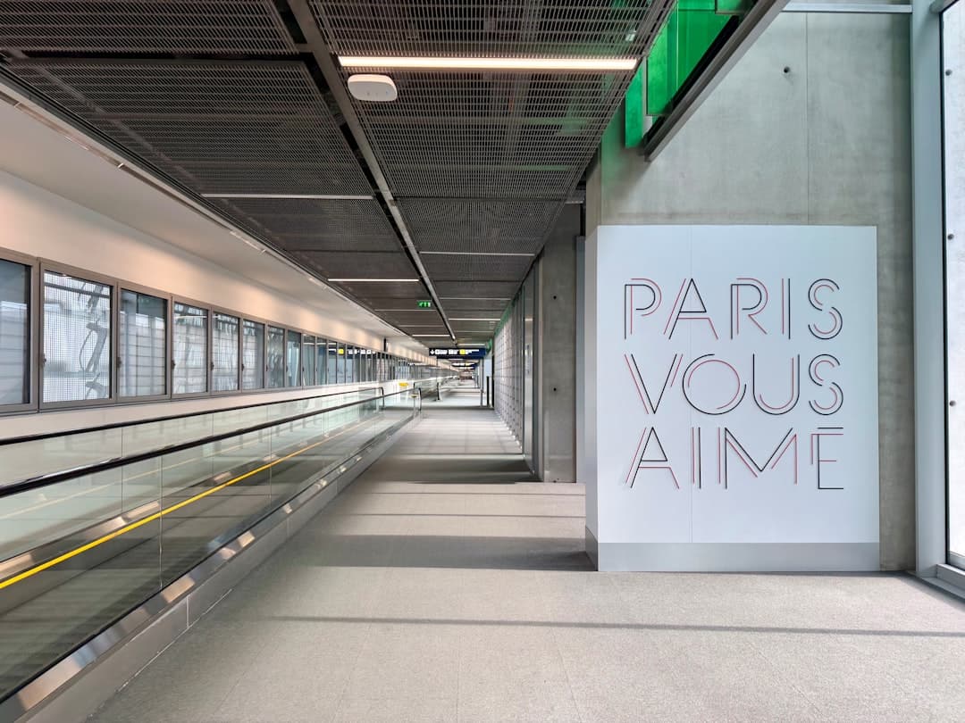 A modern, empty metro/subway station platform with escalators, contemporary architecture, and a sign reading 'PARIS VOUS AIME' (Paris Loves You) on the right wall. - Photo by John Cameron on Unsplash