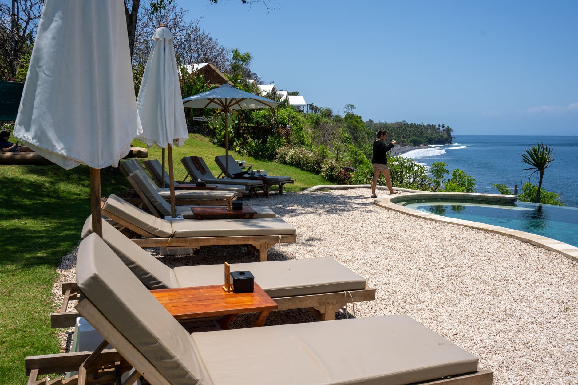 A luxury beachfront resort with infinity pool, sun loungers under white umbrellas, manicured gardens, and ocean views overlooking a tropical coastline with dense vegetation. - Photo by Tom Fisk on Pexels