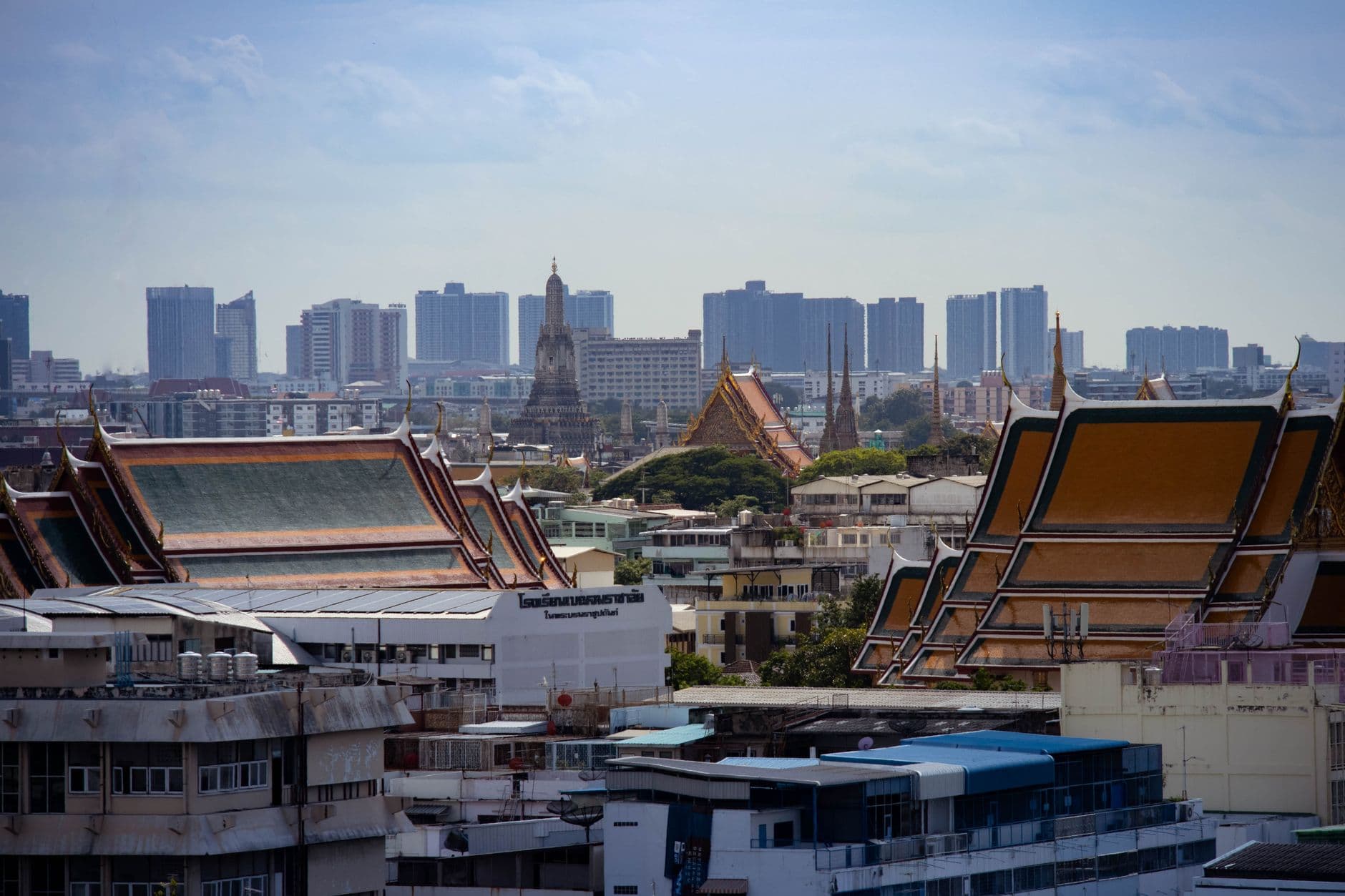 View of Bangkok's skyline from an elevated position showing ornate Thai temples in the foreground with their distinctive golden and red roofs, contrasting with modern high-rise buildings of the city center in the background. - Photo by Zaonar Saizainalin on Pexels