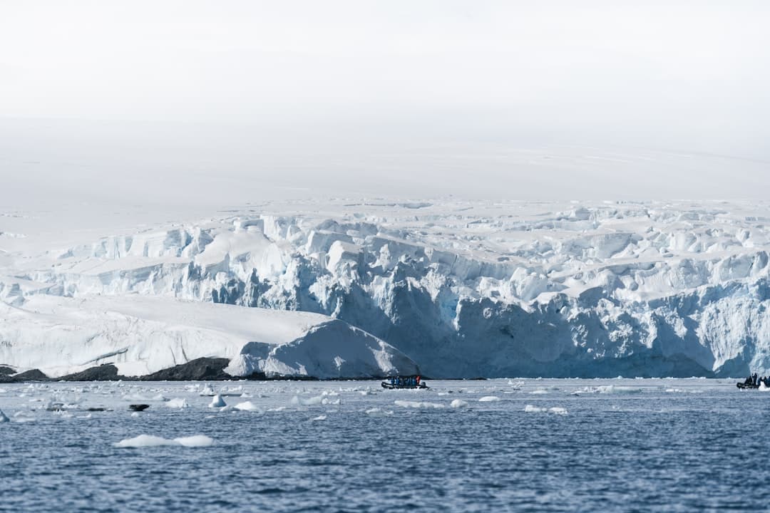 A view from the water of towering Antarctic ice cliffs with zodiac expedition boats carrying kayakers, showing the scale and majesty of glacial features in the Antarctic Peninsula region. - Photo by James Eades on Unsplash