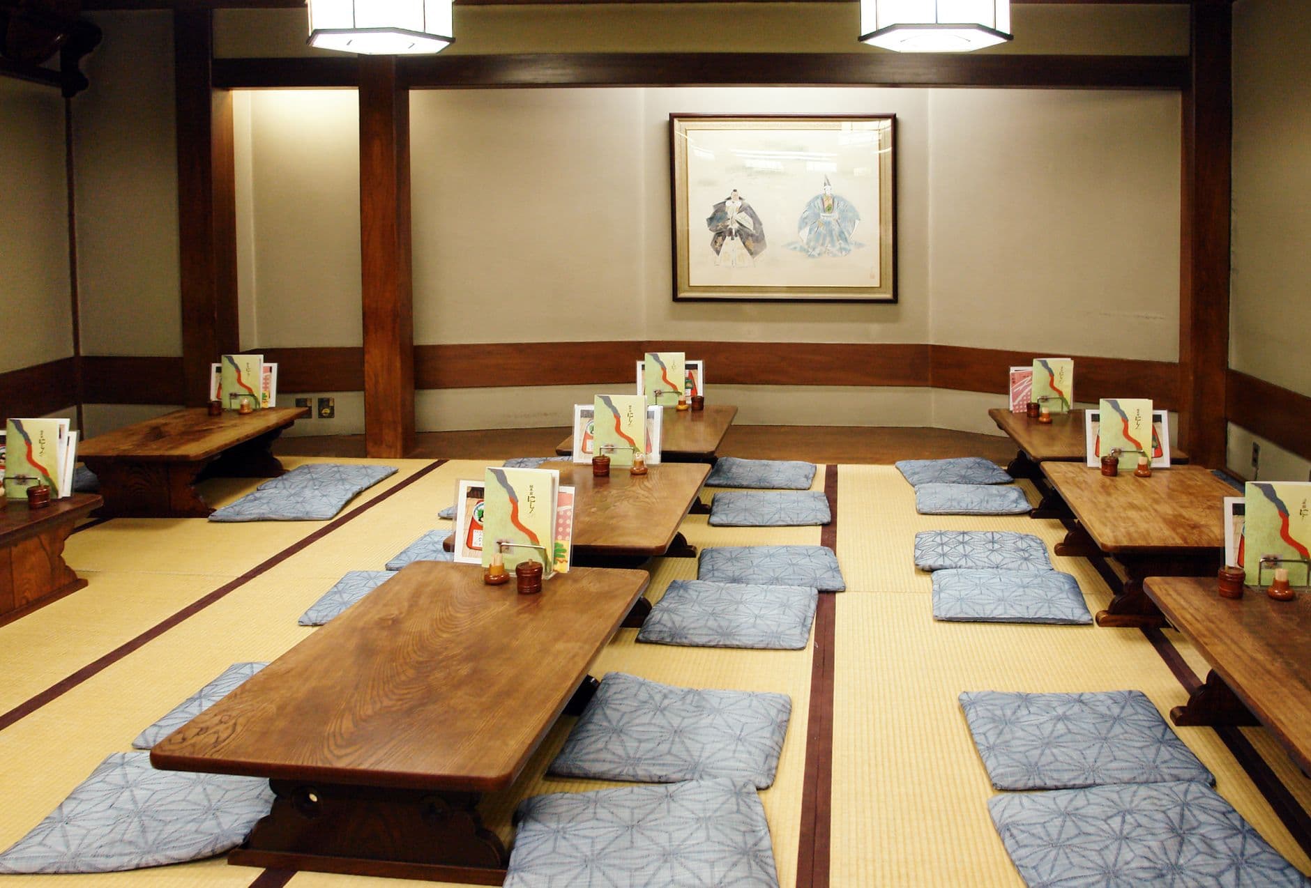 An empty private dining room in a traditional Japanese restaurant featuring low wooden tables, blue zabuton cushions, tatami mats, and authentic Japanese décor including framed bird artwork. - Photo by Bor Jinson on Pexels