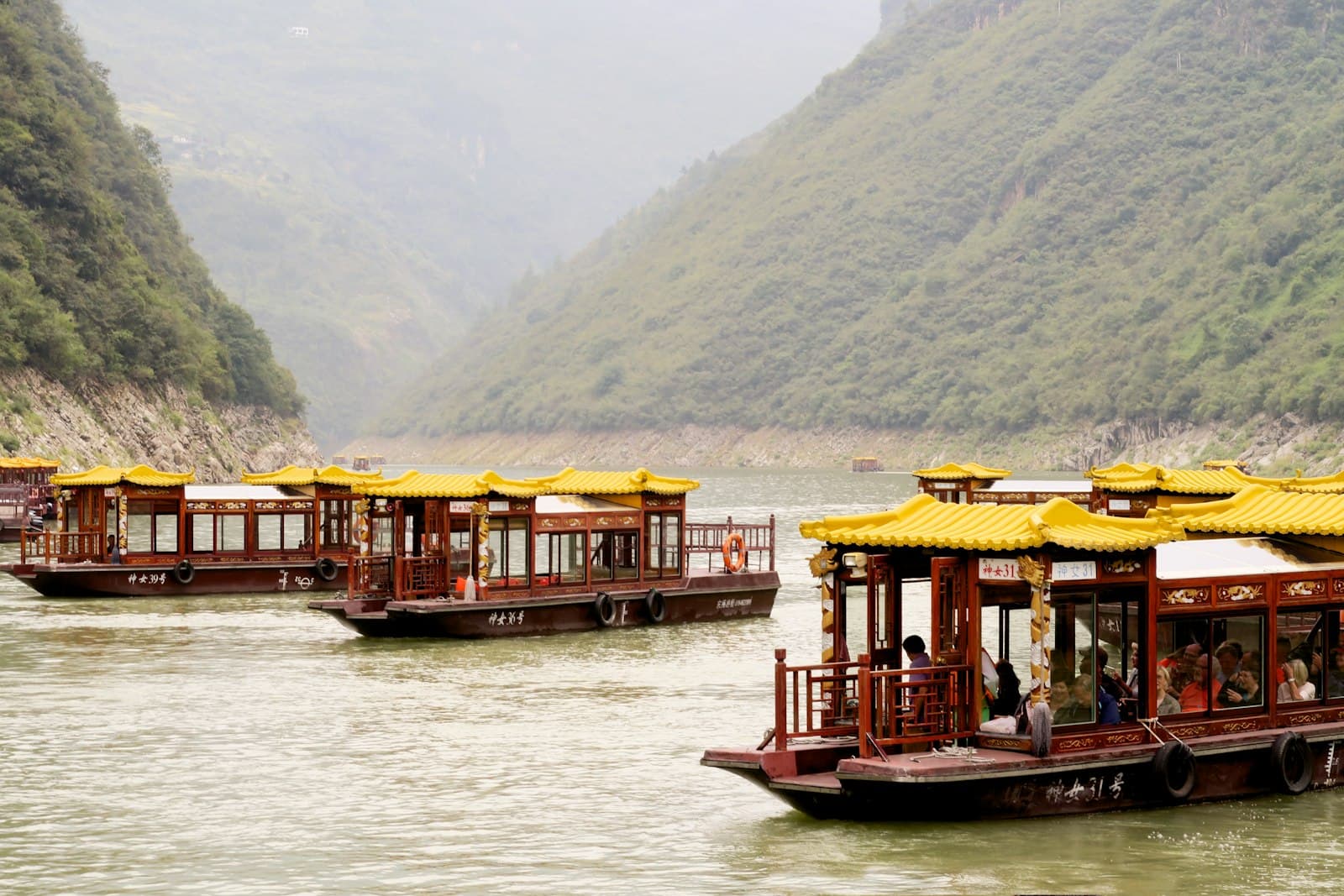 Traditional red wooden tour boats with yellow glazed-tile roofs moored on the Yangtze River with dramatic forested gorge walls rising on both sides. - Photo by Freysteinn G. Jonsson on Unsplash