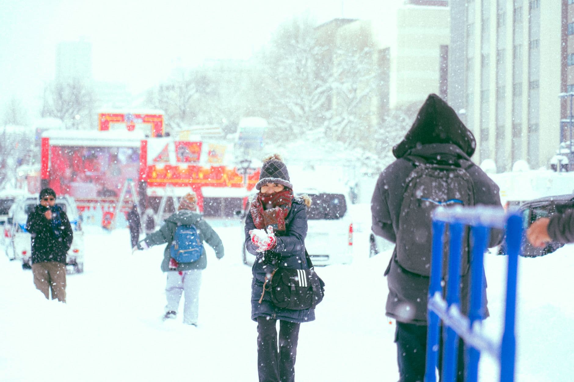 Children and adults enjoy a snowy winter festival in heavy snowfall, with red festival structures and holiday decorations visible in the background of what appears to be a major public plaza. - Photo by travelers_tw on Pexels