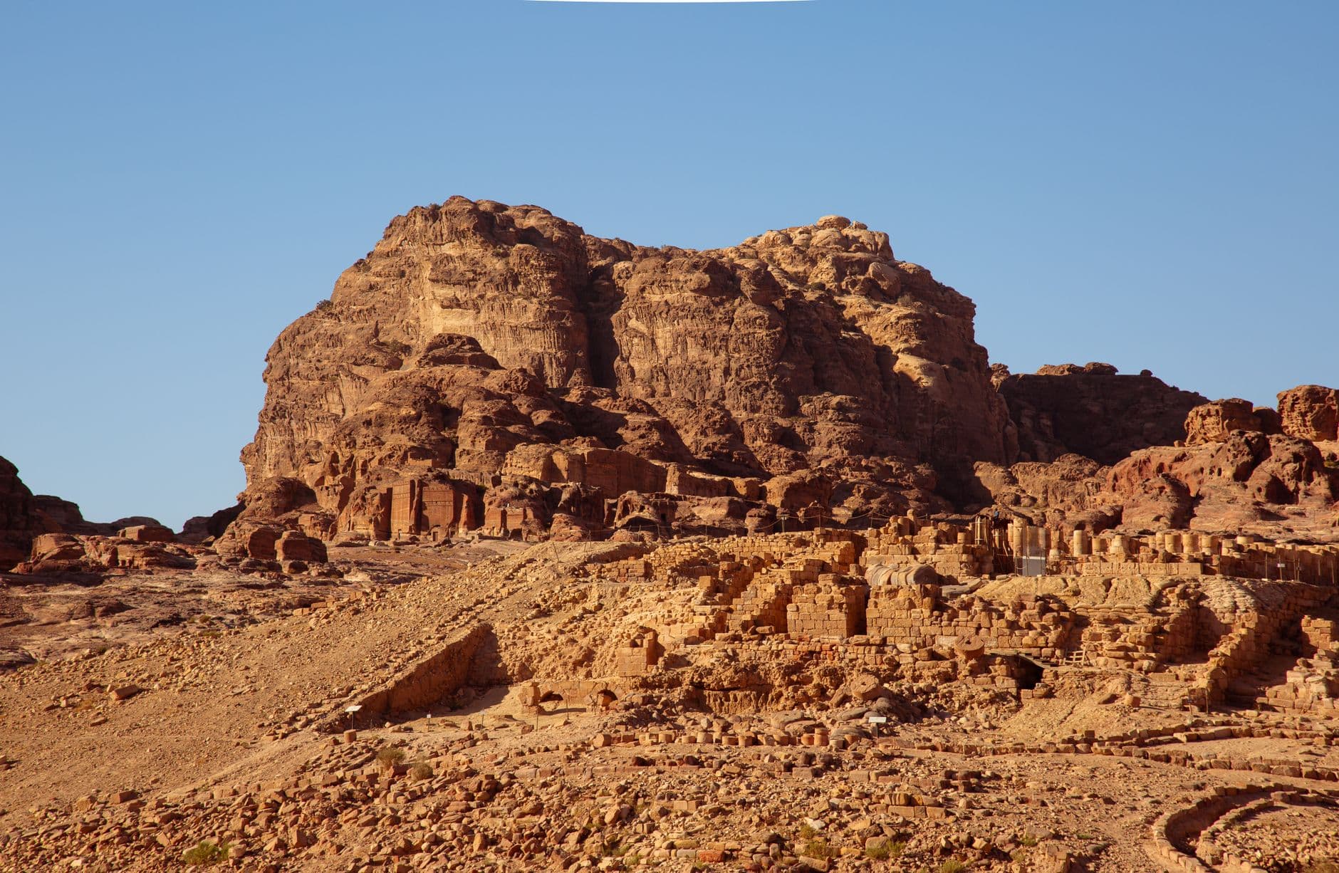 Ancient Nabataean ruins at Petra, Jordan, showing carved stone structures and facades built into and carved from the rose-red sandstone cliffs under clear desert skies. - Photo by Yousef salah on Pexels