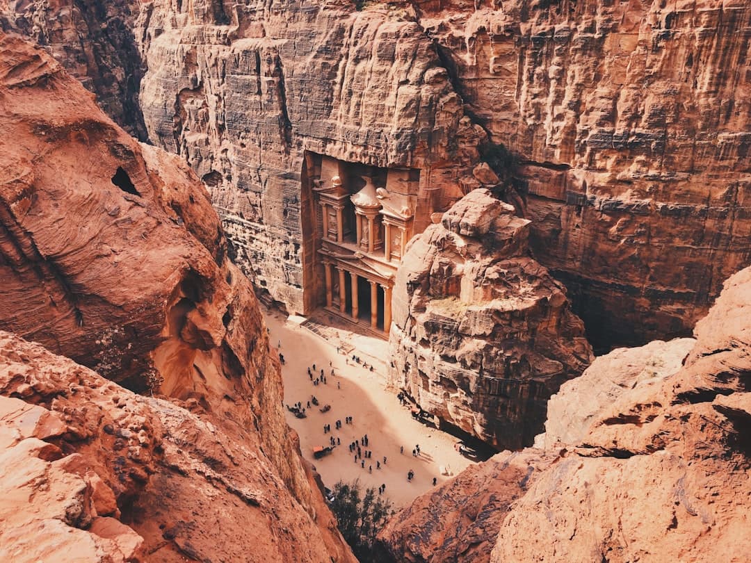 An aerial view of Al-Khazneh (The Treasury), Petra's most famous monument, showing the ornate Nabatean-carved facade nestled in a narrow canyon with tourists gathered at its base. - Photo by Alex Vasey on Unsplash
