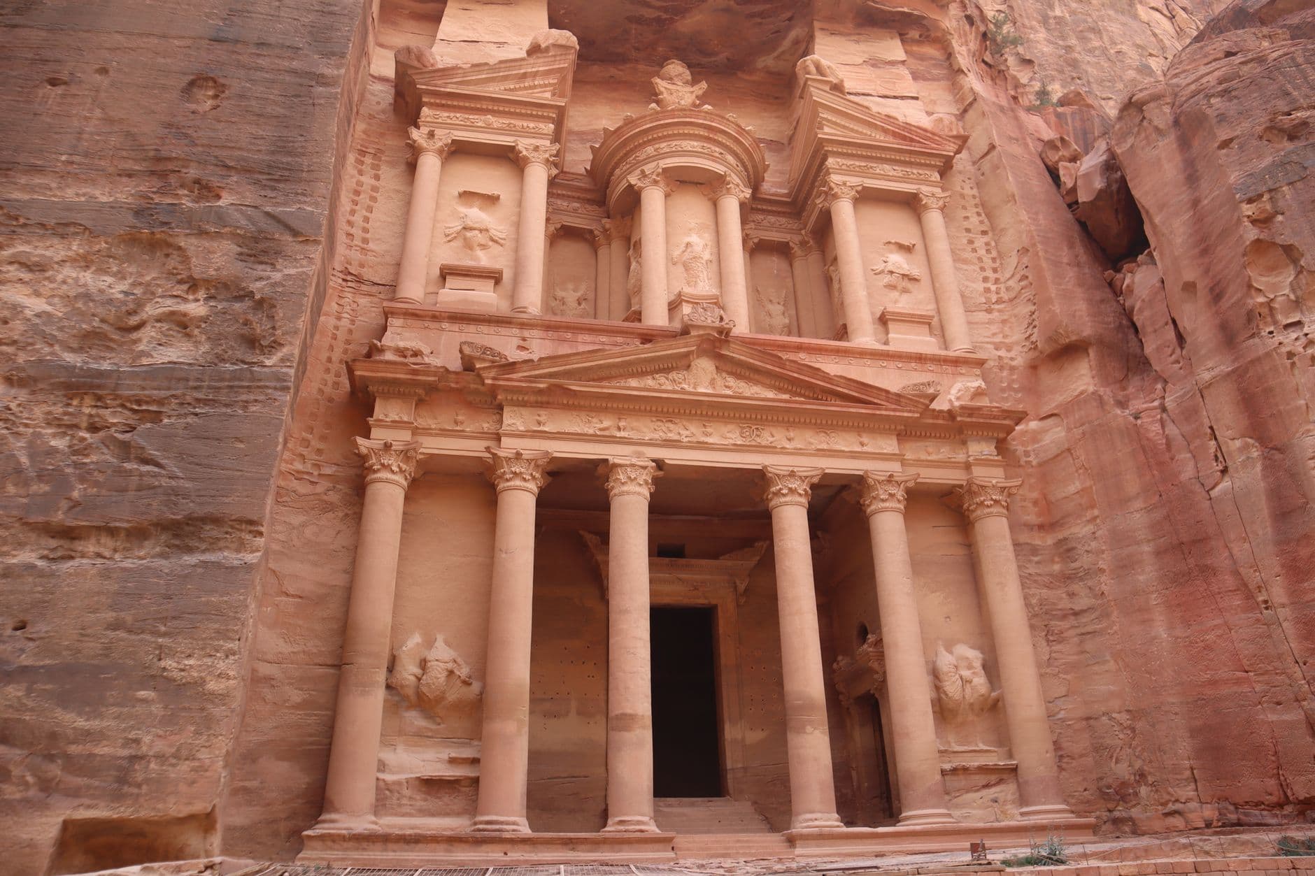 The carved facade of Al-Khazneh at Petra, a monumental Nabatean temple carved from rose-red sandstone featuring two tiers with Corinthian columns and ornamental detailing. - Photo by Mihaela Claudia Puscas on Pexels