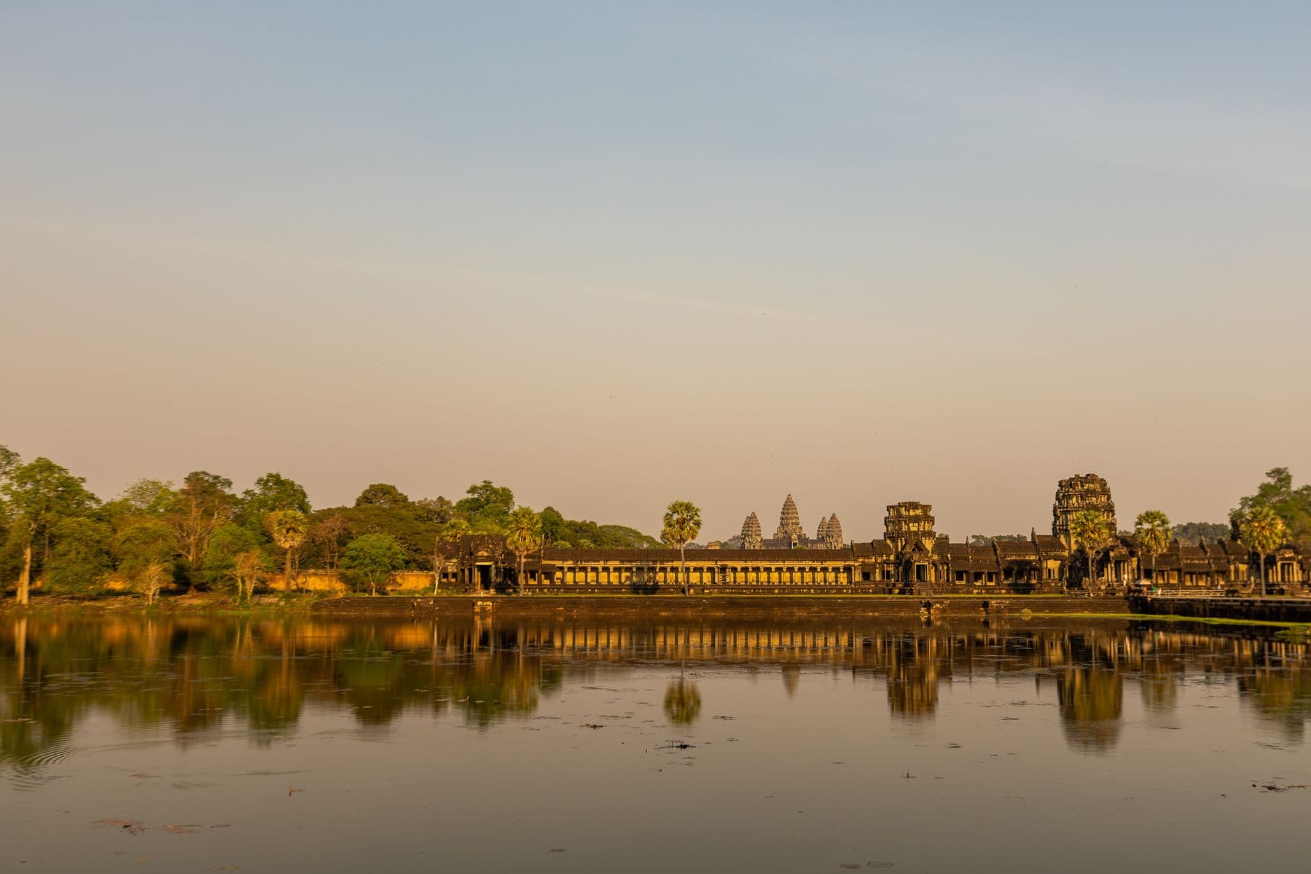 Angkor Wat temple complex in Siem Reap, Cambodia, photographed from across the moat at dawn or dusk, showing the main sanctuary with its five towers and surrounding structures reflected in still water. - Photo by Serg Alesenko on Pexels