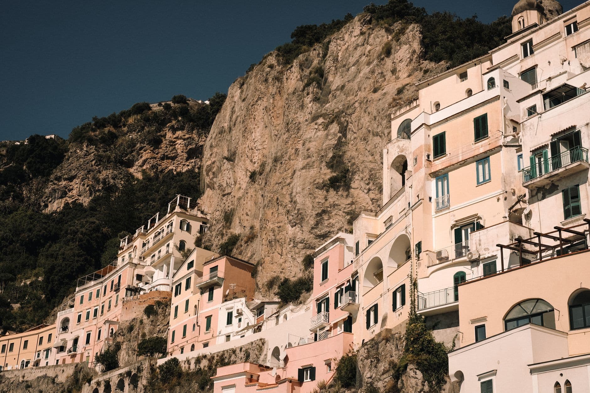 Cliffside village with pastel-colored buildings built into limestone cliffs, featuring Mediterranean architecture with arched windows, green shutters, and terraced construction on a steep coastal slope. - Photo by Alina Chernii on Pexels