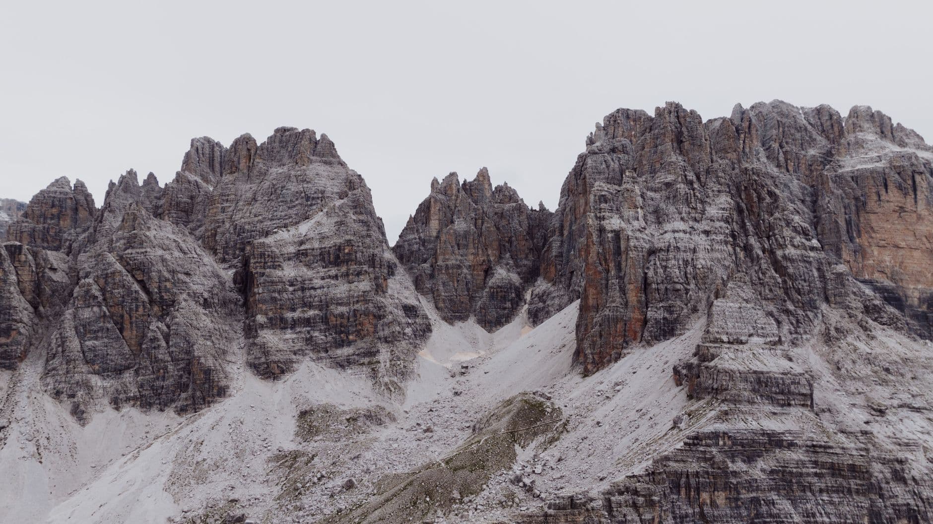 A snow-covered alpine landscape featuring distinctive columnar dolomitic limestone towers and peaks characteristic of the Dolomites, with partial snow coverage on the scree slopes and lower elevations. - Photo by K on Pexels