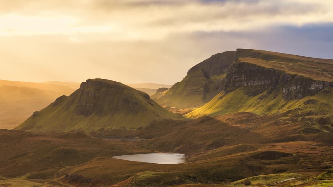 Alpine moorland landscape with distinctive flat-topped mountains, a small lochan (mountain pool), and golden-hour lighting illuminating the characteristic Scottish Highlands terrain. - Photo by Jonas on Unsplash