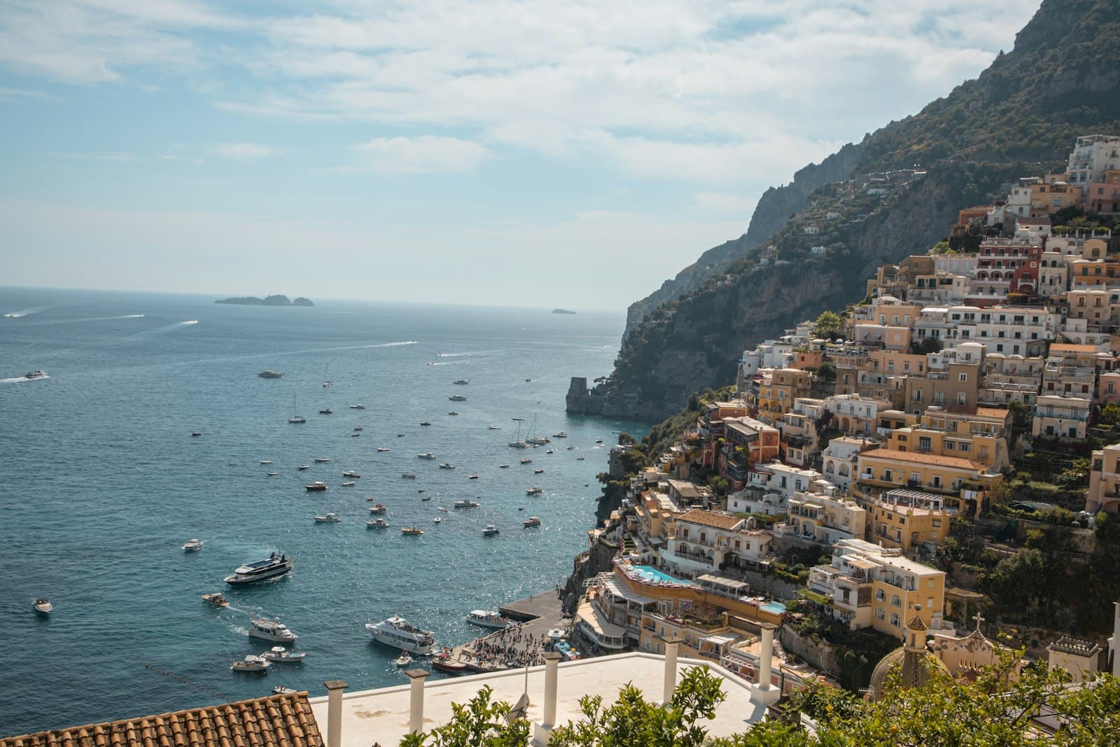 A clifftop view of Positano's densely packed colorful buildings cascading down a steep coastline to a turquoise Mediterranean bay dotted with moored boats. - Photo by Wyatt Simpson on Unsplash