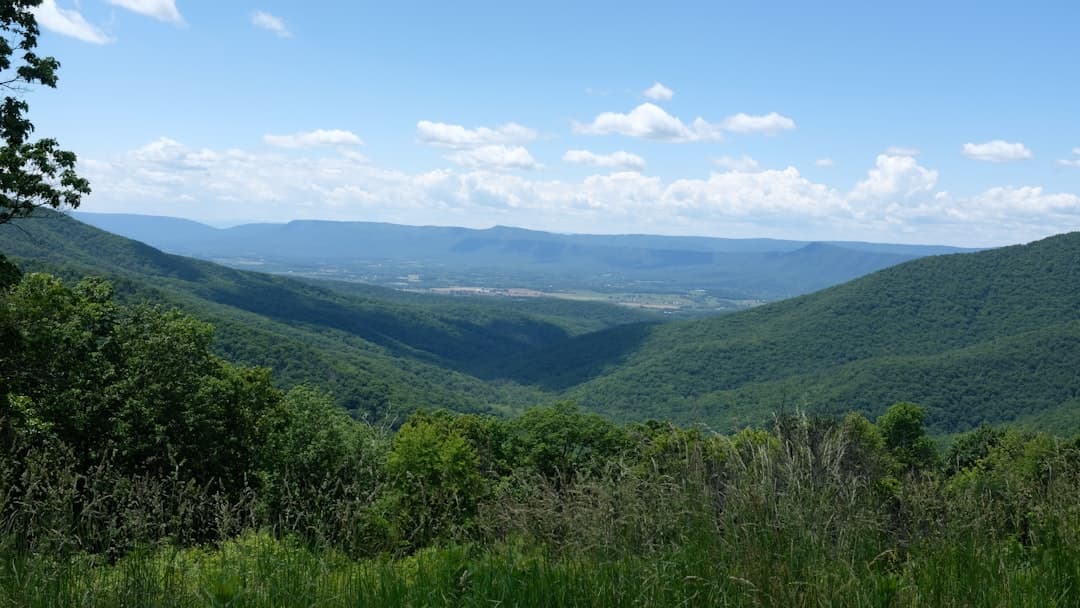 A panoramic view from a high elevation looking down into a deep valley between forested mountain ridges, with cultivated fields visible on the valley floor and misty ridgelines in the distance. - Photo by Girma Nigusse on Unsplash