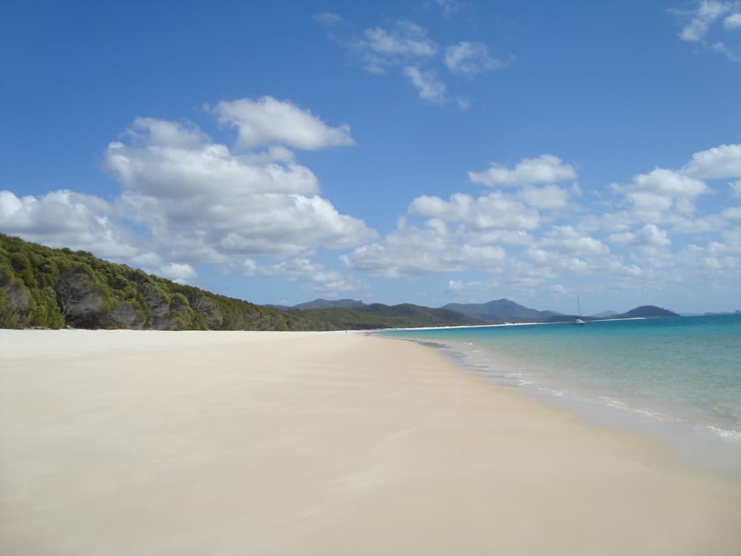 A pristine white sand beach with turquoise waters, rocky vegetated headland, and multiple islands visible across the tropical seascape. - Photo by Alison Voyager on Unsplash