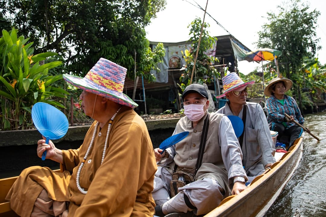 Tourists in a wooden sampan boat on a waterway in the Mekong Delta, with local boatmen wearing traditional conical hats and casual clothing, surrounded by tropical vegetation and stilted dwellings. - Photo by Leo_Visions on Unsplash